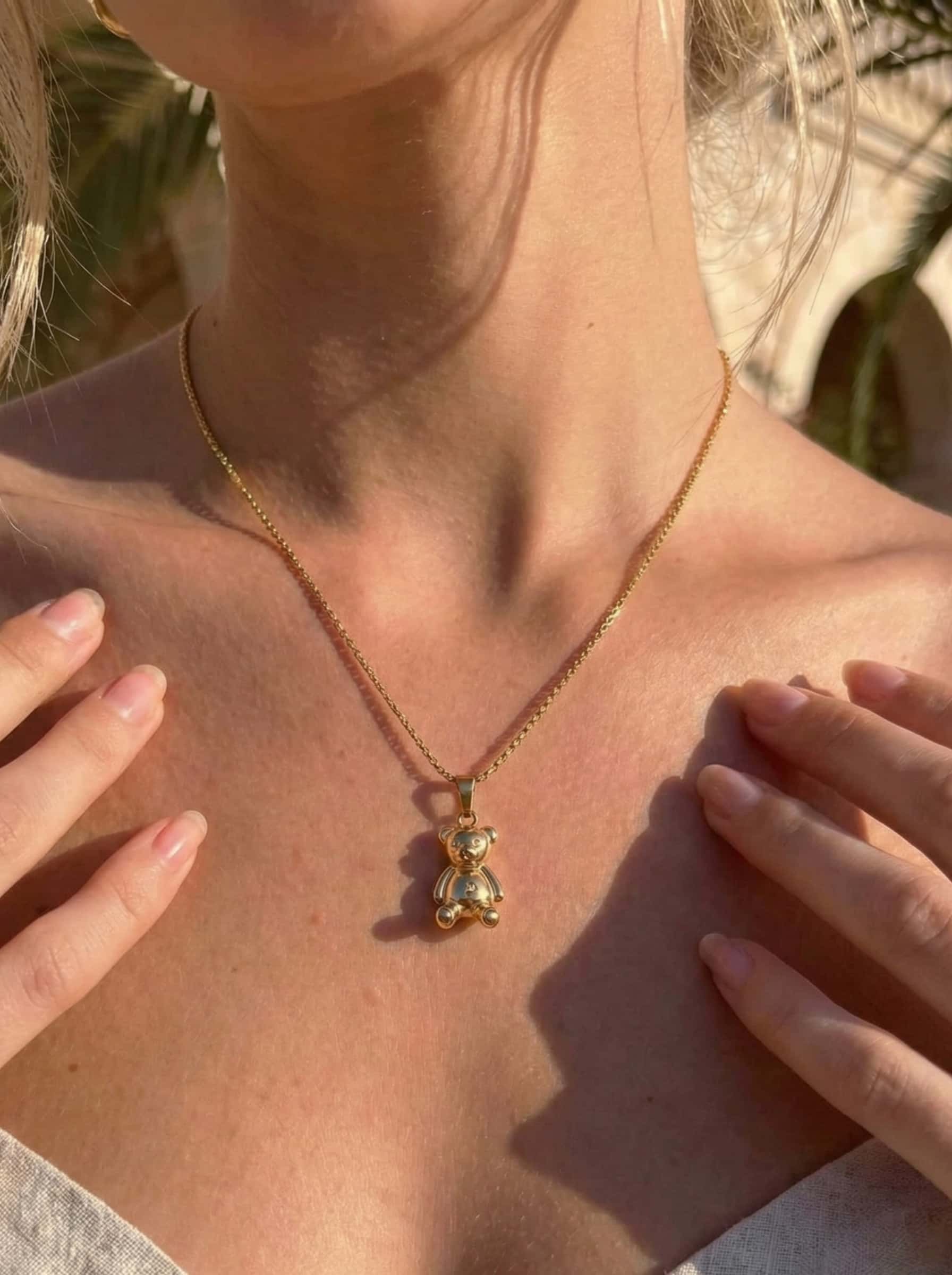 Gold necklace with a teddy bear pendant worn by a person outdoors