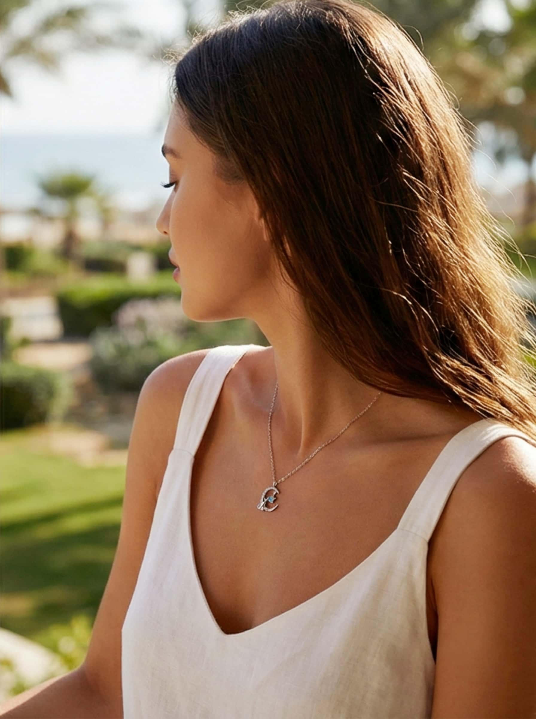 Profile of a woman outdoors modeling a delicate cat necklace, demonstrating how the elegant silver chain and pendant complement a sunny, natural aesthetic.