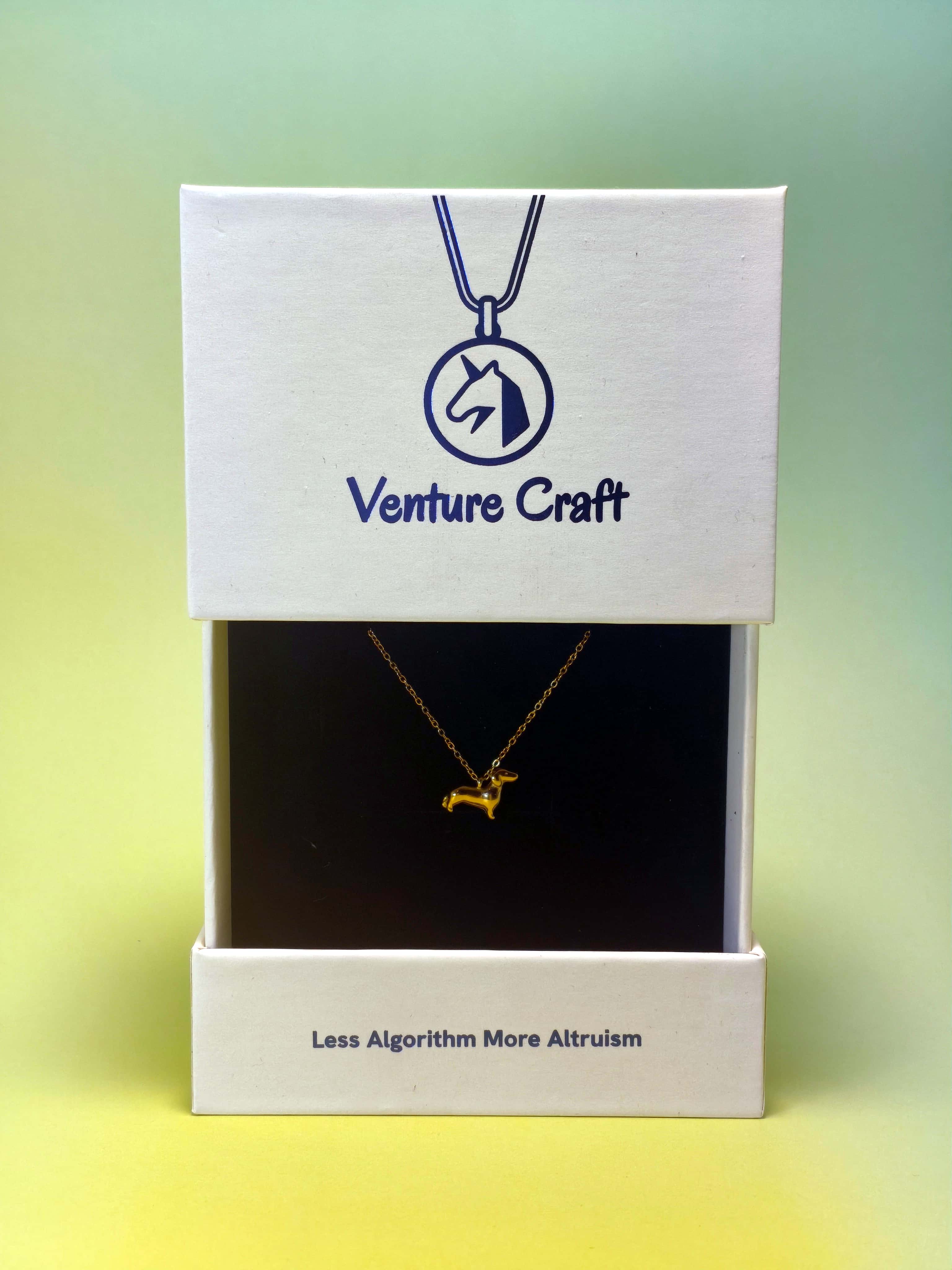 Gold dachshund necklace in a Venture Craft gift box with a gradient background