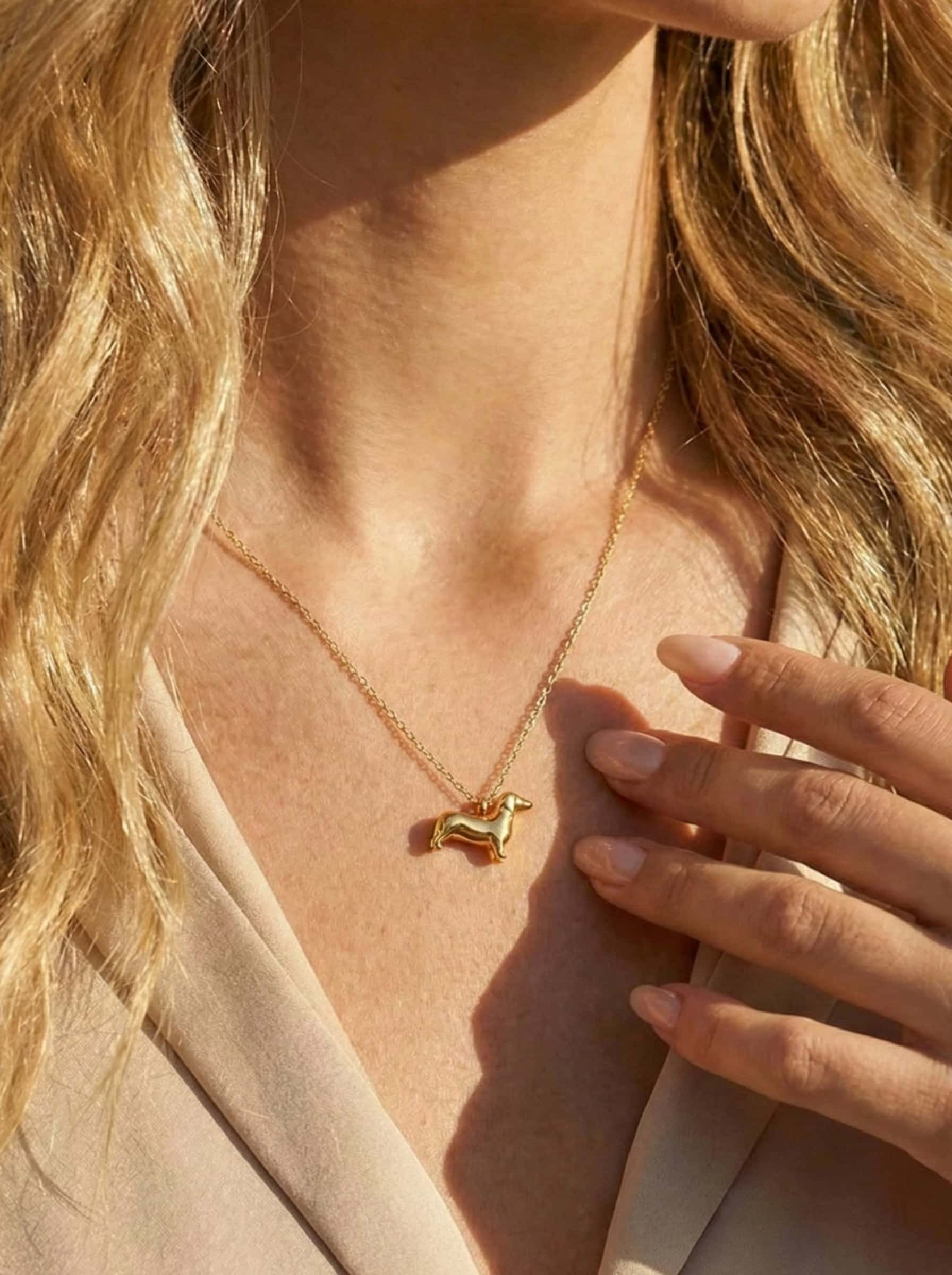 Gold necklace with a small dog-shaped pendant worn by a person with blonde hair.