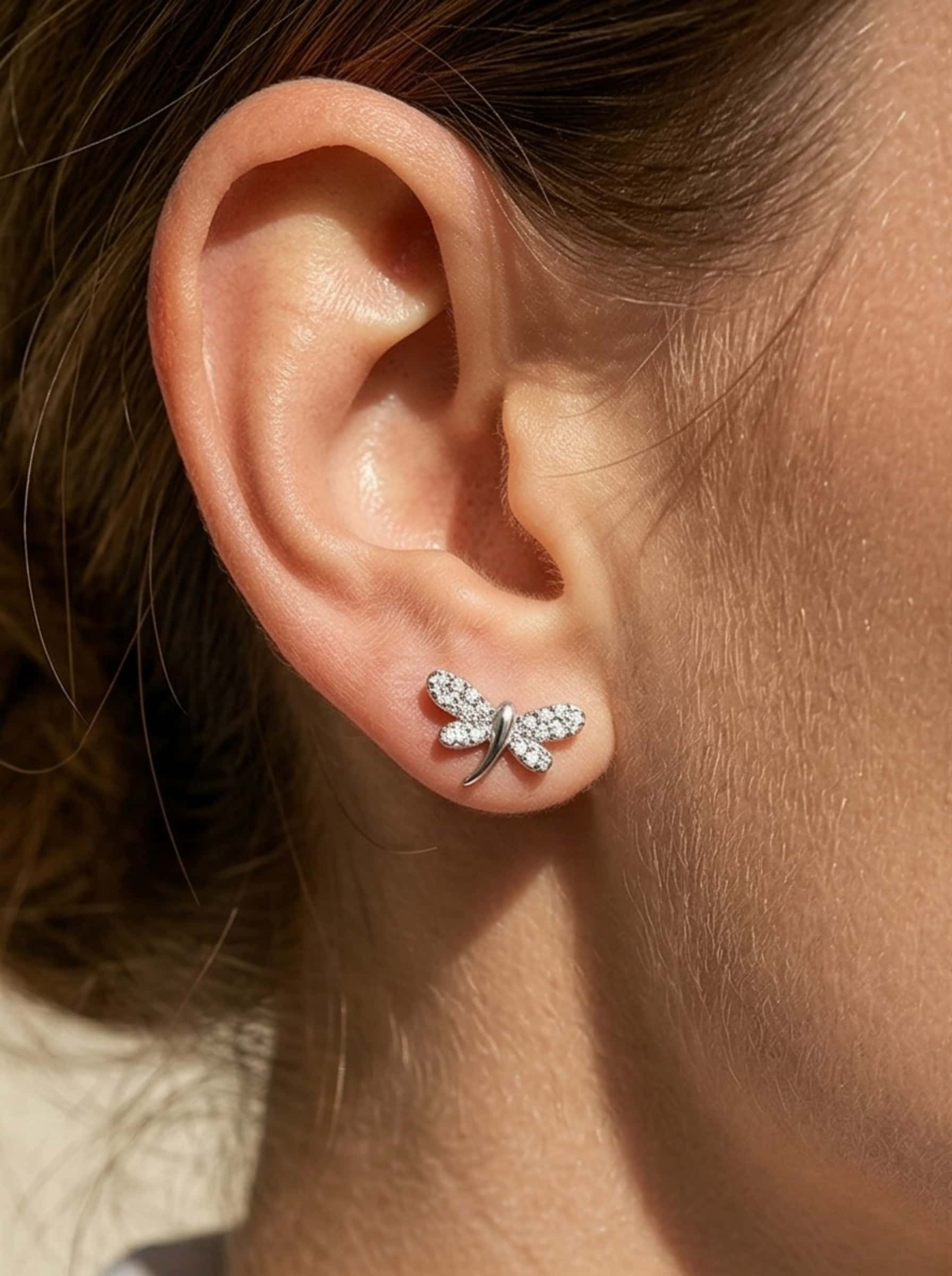 Close-up detail of delicate dragonfly stud earrings worn beautifully on the ear.