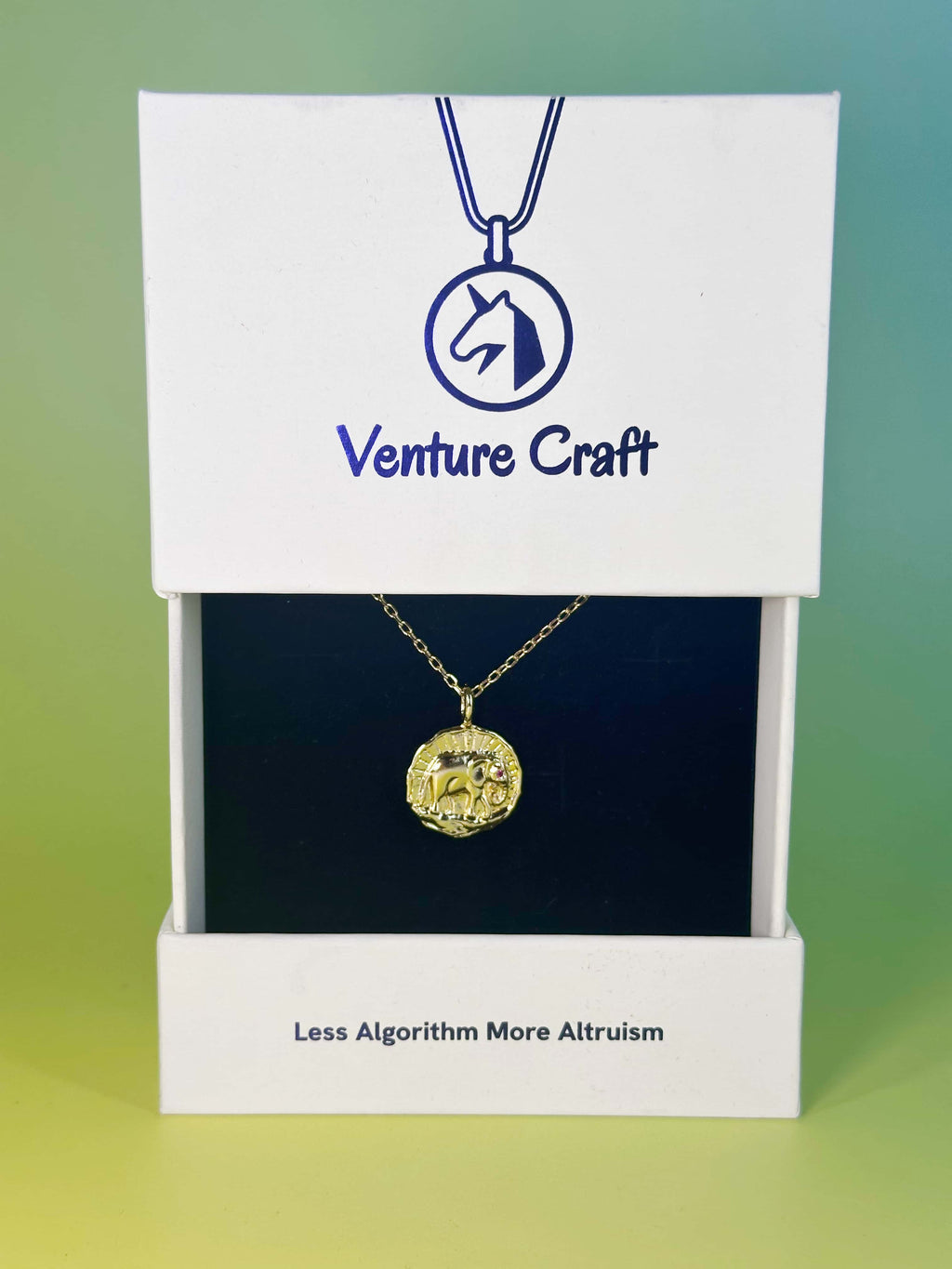 The 18K gold elephant necklace beautifully presented inside the signature white and black Venture Craft gift box on a gradient background