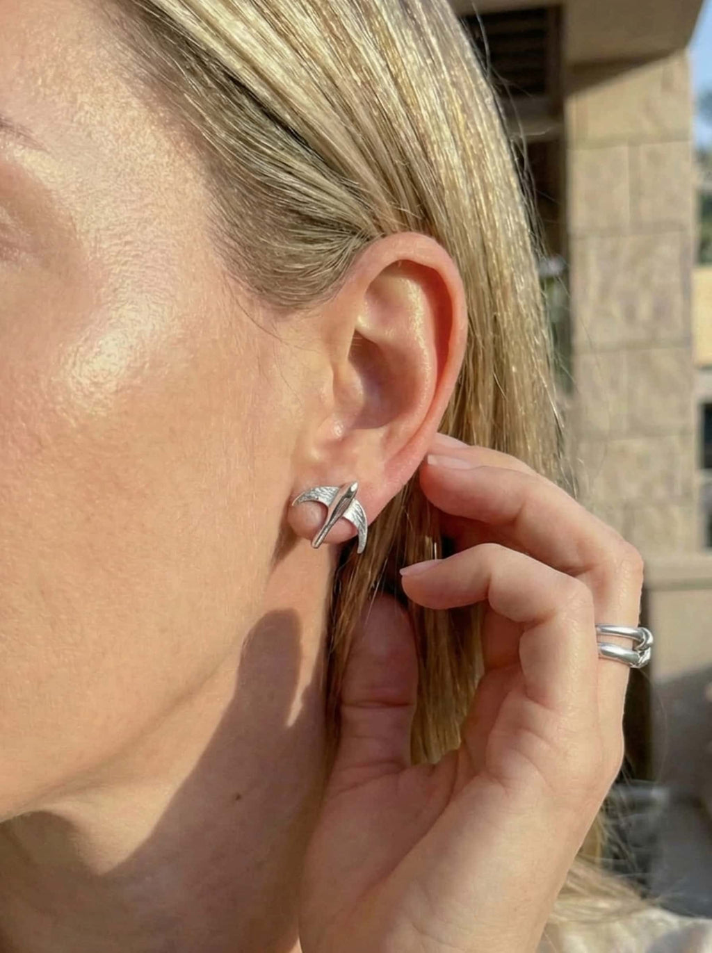 Close-up of a person wearing a silver bird stud earrings with a building in the background