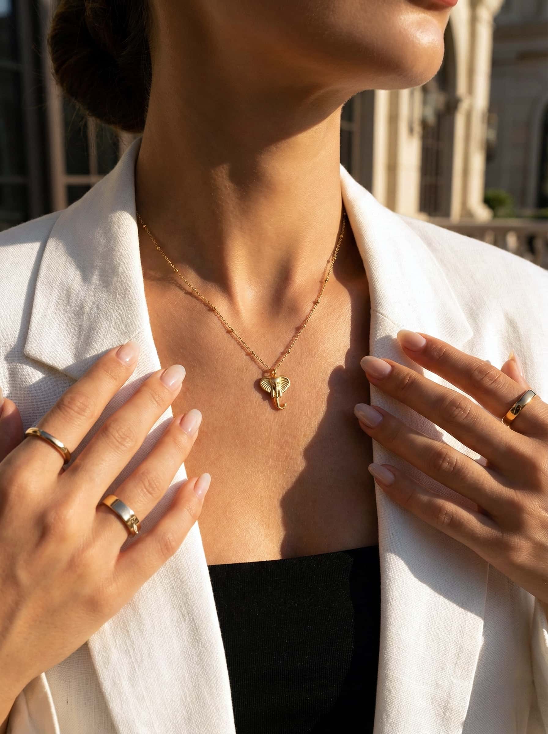 Person wearing a gold necklace with a heart pendant, holding their hands near their face.