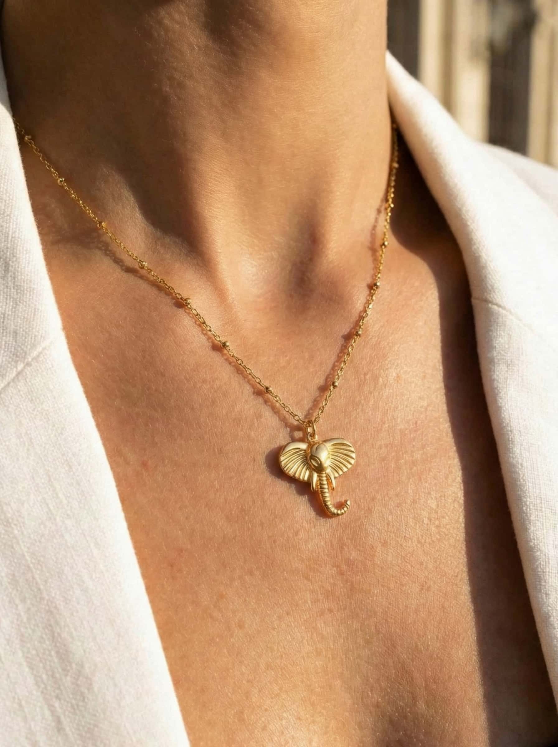 Gold necklace with a elephant-shaped pendant on a person wearing a white shirt.